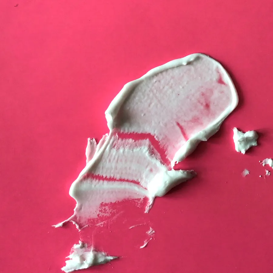 Creme de barreira branco passado num traço sobre acrílico rosa, visto de cima