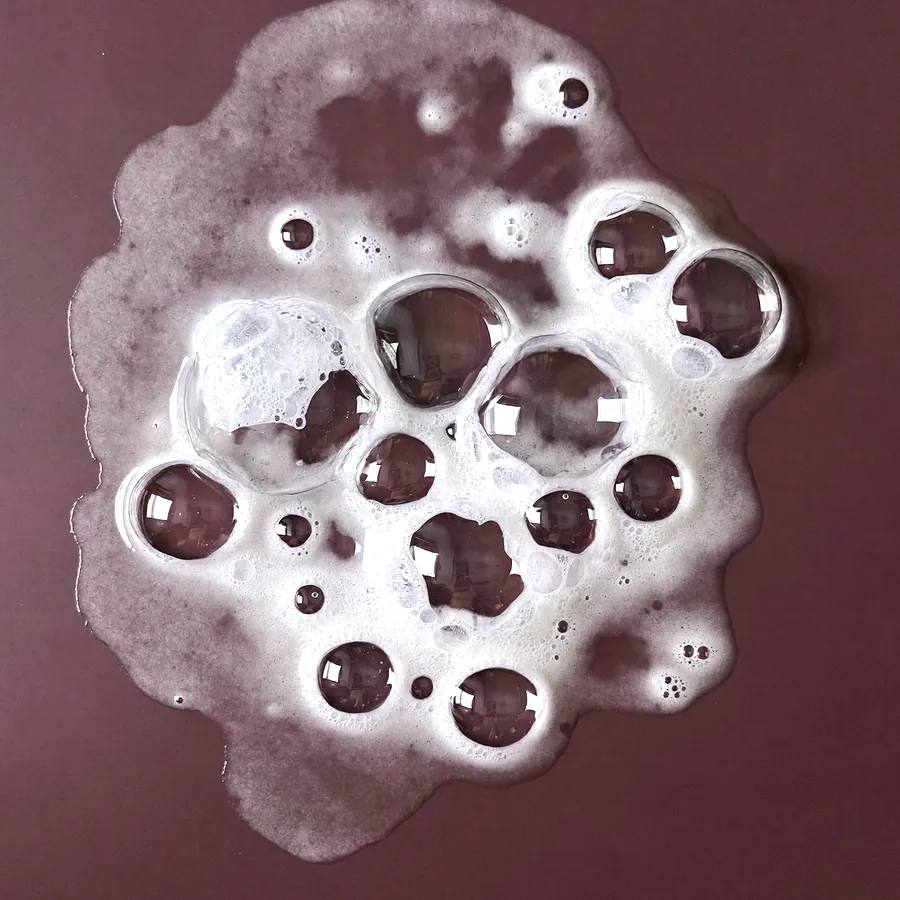 Espuma branca de limpeza com bolhas de vários tamanhos sobre acrílico roxo-escuro, vista de cima